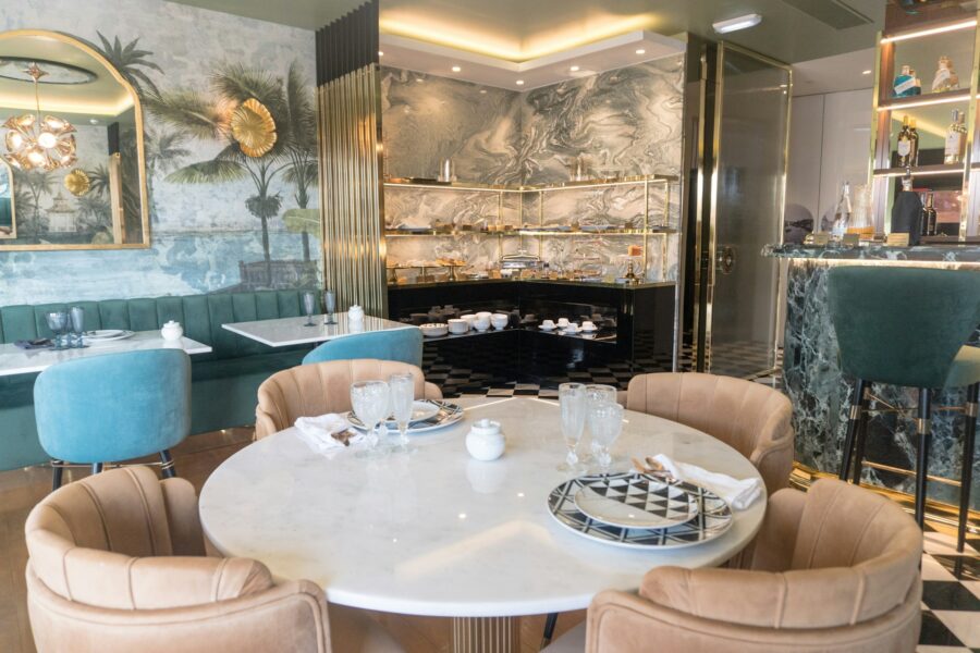 Chic modern restaurant interior with tropical motifs, marble table, plush chairs, and elegant bar.