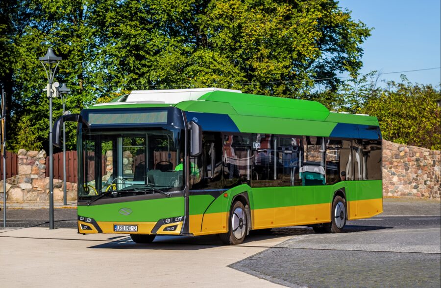 Modern green and yellow city bus parked in sunny urban park setting.