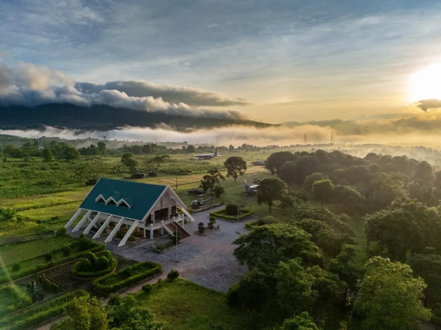 Modern hillside building at sunrise overlooking misty mountains, lush green fields and rural landscape.