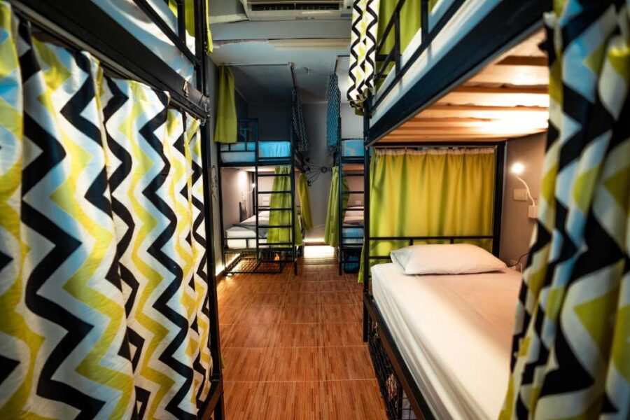 Modern hostel dorm room with metal bunk beds, privacy curtains, wooden floor, and shared accommodation.
