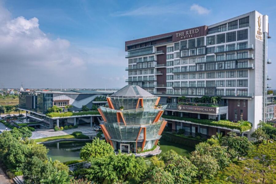 Modern luxury hotel and medical spa resort with glass pavilion and pond in lush landscaped grounds.