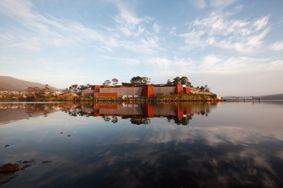 Modern waterfront museum architecture reflected in calm lake at sunset, contemporary rust-colored building.