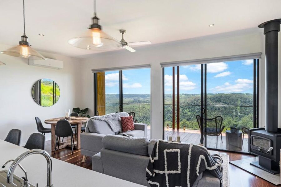 Modern open plan living room with hillside view, large windows, balcony, and contemporary furniture.