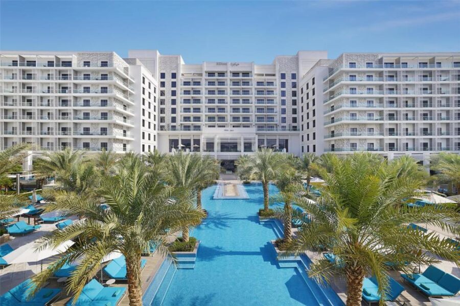 Luxury Abu Dhabi beachfront resort with infinity pool, palm trees, and modern white hotel building.