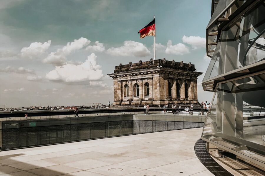 Historic German building with flag, modern balcony, sky, clouds, people, architectural contrast.