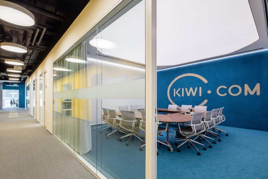 Modern Kiwi.com office hallway with glass-walled conference rooms and blue accent wall.