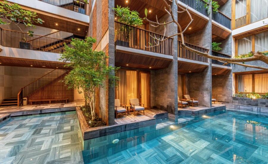 Luxury boutique hotel courtyard with modern pool, private terraces, balconies, and tropical evening lighting.