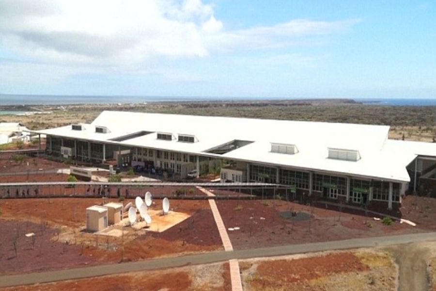 Modern research facility with white roof, satellite dishes, rugged landscape, and ocean backdrop.