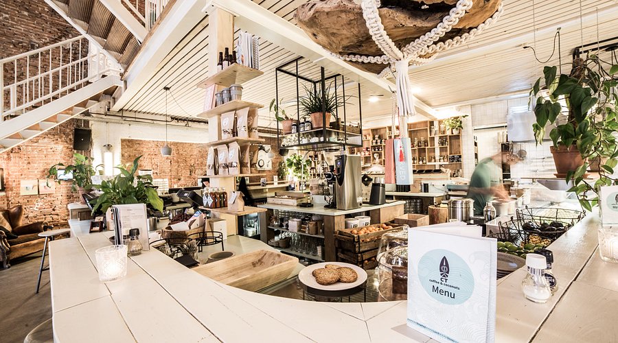 Modern rustic cafe interior with white counter, plants, spiral staircase, barista, cozy coffee shop decor.