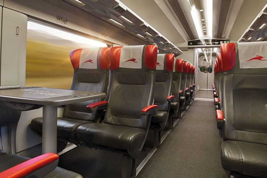 Modern train compartment with sleek design, dark grey leather seats, red details, and large windows.