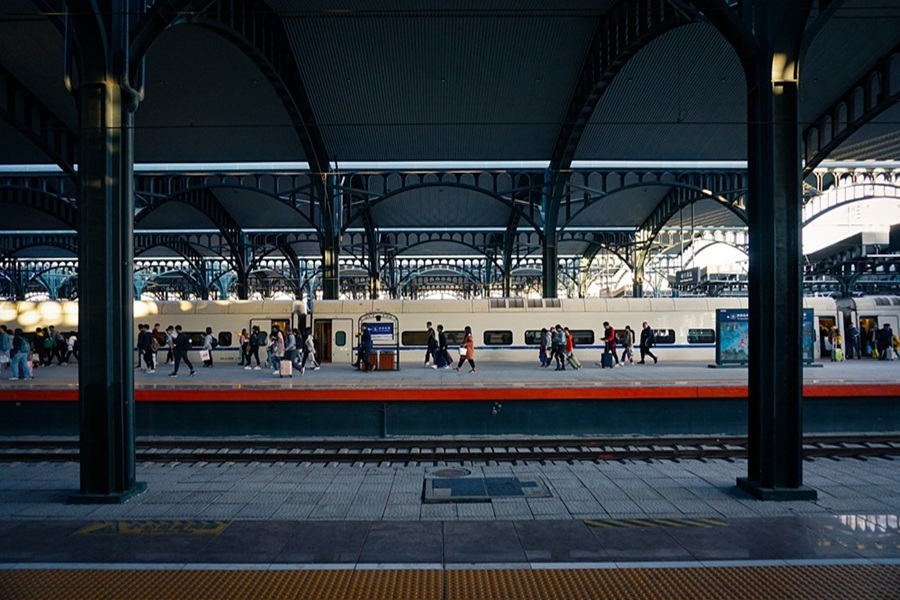 Bustling train station with diverse travelers, modern train, and historical architecture.