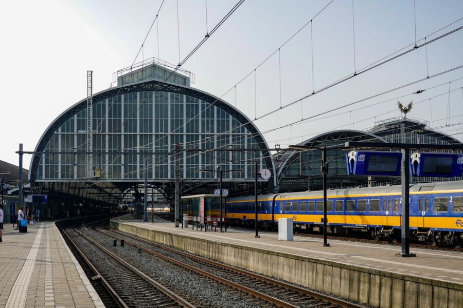 Modern glass and steel railway station with yellow train, passengers, and informational displays.