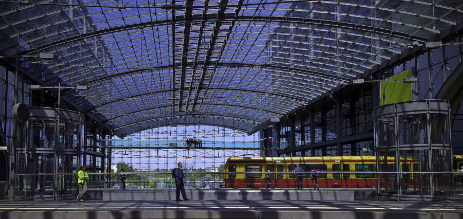 Futuristic railway station with glass ceiling, bustling commuters, and colorful train enhancing urban connectivity.