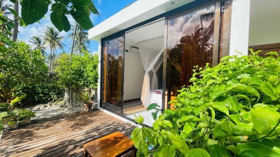 Modern tropical bungalow villa with wooden deck, glass doors, lush greenery and serene island retreat.