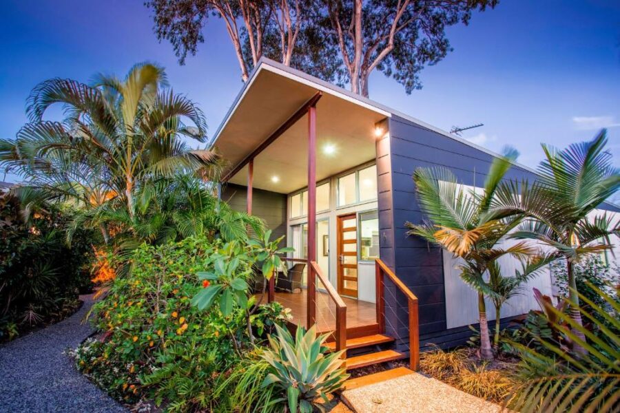 Modern tropical holiday park cabin at twilight surrounded by lush palm trees and garden.