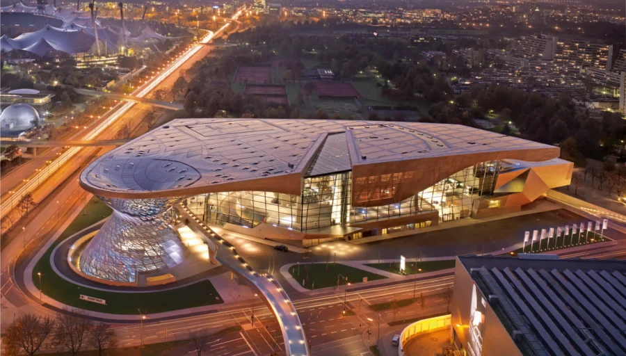 BMW Welt aerial view at dusk showing modern glass roof cultural complex and illuminated highways.