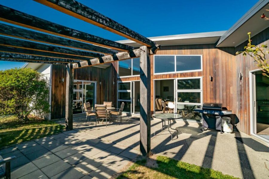 Modern wooden backyard patio with pergola, outdoor dining area, barbecue grill, and contemporary home.