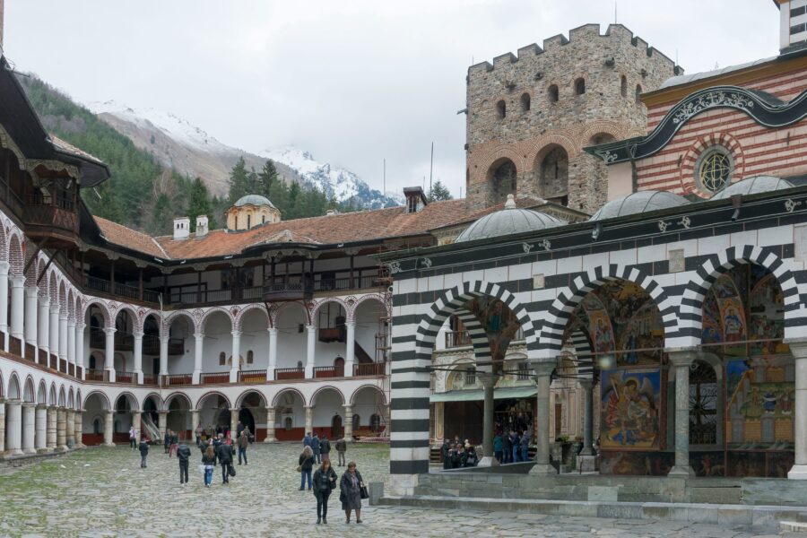 Rila Monastery courtyard in Bulgaria with striped arches, frescoes, tower and mountain backdrop.