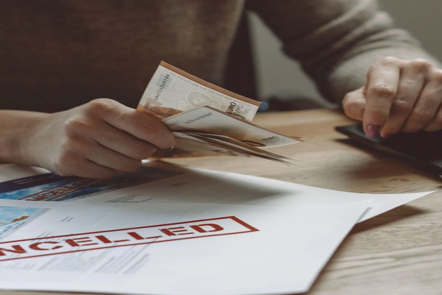 Person handling cash with cancellation document on wooden table, reflecting tension and contemplation.