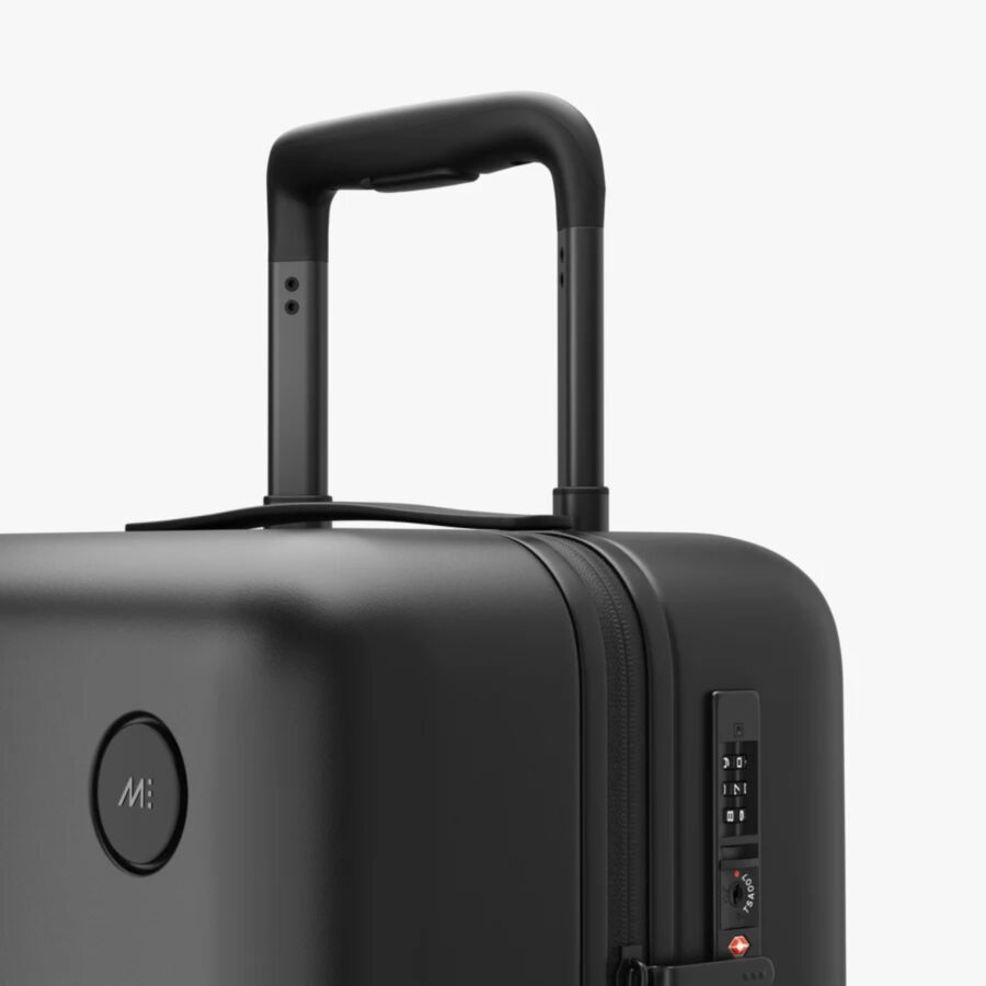 Close-up of a Monos Carry-On black suitcase featuring a telescopic handle, combination lock, and zippered closure, conveying modernity and security.