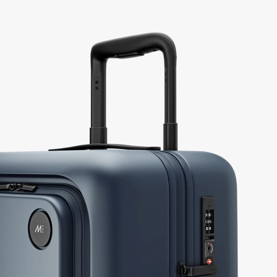 Close-up of a blue Monos Carry-On Pro suitcase with wheels, set against a white background.