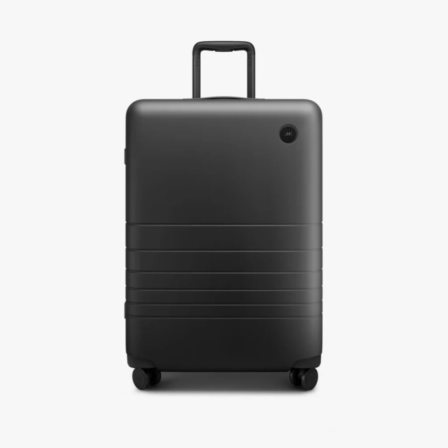 Monos Check-In Medium with horizontal grooves and a retractable handle. It has four wheels, conveying a modern and minimalist design.