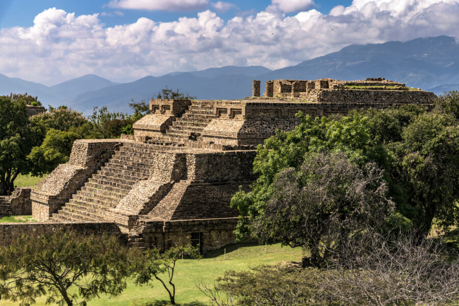 Scenic view of Monte Alban Temple, featuring ancient stone architecture atop a hill with lush greenery in the background.
