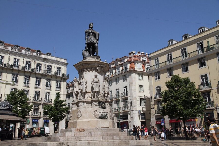 Luis de Camoes monument in Lisbon square, people, historic buildings, bright blue sky.