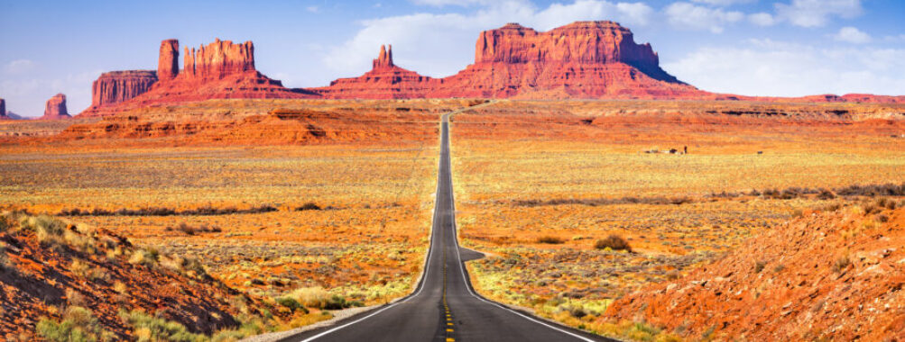 Scenic view of a winding road through Monument Valley, showcasing iconic red rock formations under a clear blue sky.