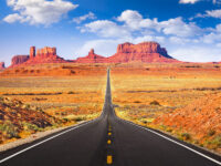 Scenic view of a winding road through Monument Valley, showcasing iconic red rock formations under a clear blue sky.