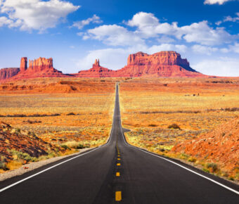 Scenic view of a winding road through Monument Valley, showcasing iconic red rock formations under a clear blue sky.