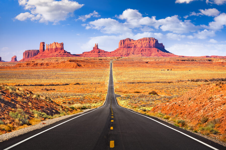 Scenic view of a winding road through Monument Valley, showcasing iconic red rock formations under a clear blue sky.