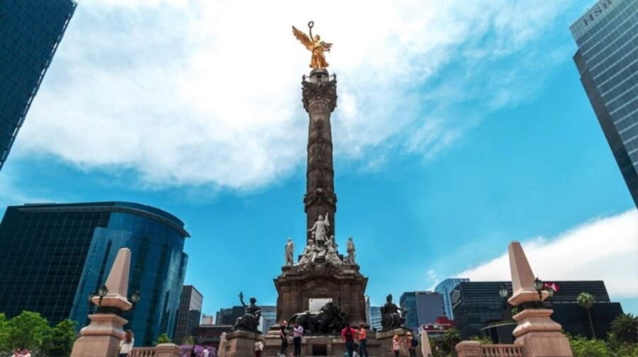 Angel of Independence monument in Mexico City with skyscrapers and visitors in vibrant sunlight.