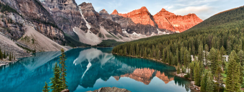 Sunrise over Moraine Lake in Banff National Park, showcasing vibrant colors reflecting on the calm water and surrounding peaks.