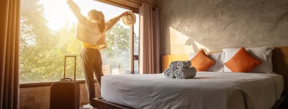 Traveler enjoying morning sunshine in modern hotel room with lush view and stylish design.