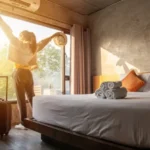 Traveler enjoying morning sunshine in modern hotel room with lush view and stylish design.
