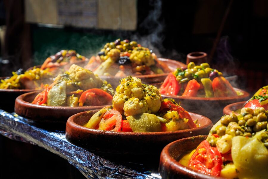 Traditional Moroccan tagines with colorful vegetables, herbs, and spices in clay pots.