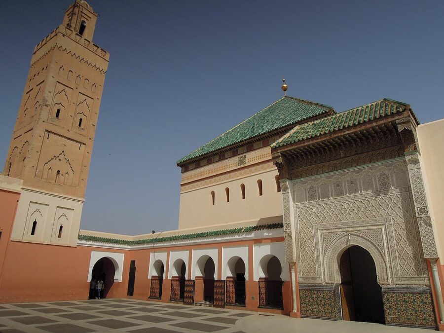 Moroccan mosque complex with ornate minaret and green-tiled building under clear blue sky.