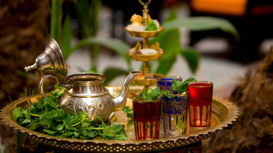 Moroccan tea set with ornate teapot, colorful glasses, and mint leaves on a tray.