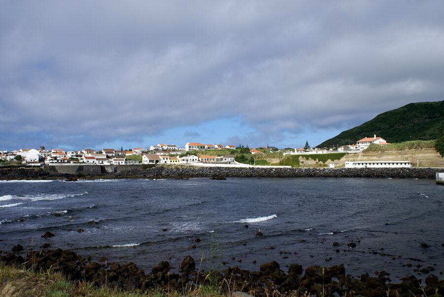 Tranquil waters of Mosteiros, São Miguel Island, reflecting the sky and framed by rugged cliffs and vibrant vegetation.