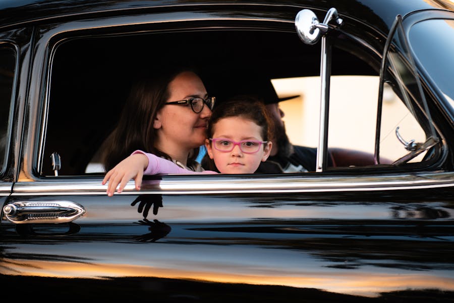 Mother and daughter bonding in vintage car during sunset, evoking warmth and nostalgia.