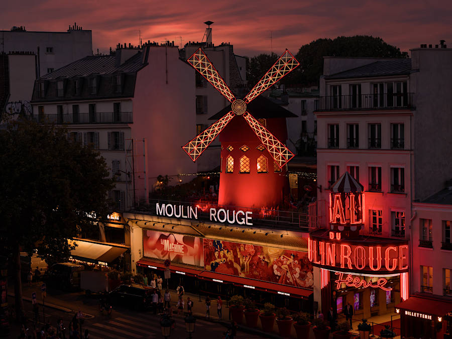 Moulin Rouge windmill and neon cabaret facade in Paris at night.