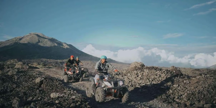 Two people riding ATVs on a rocky trail during the Mount Batur Quad Adventure at sunrise.
