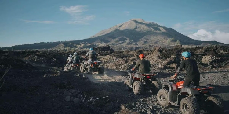 Four people riding ATVs on dirt with Mount Batur in the background during a sunrise adventure.
