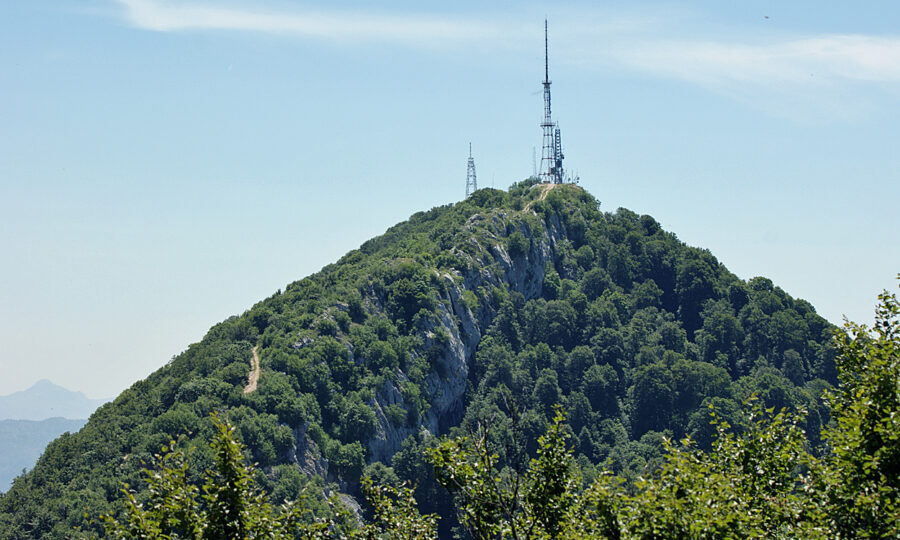 Mount Dajti stands tall with a radio tower on its summit, surrounded by lush greenery and a bright sky.