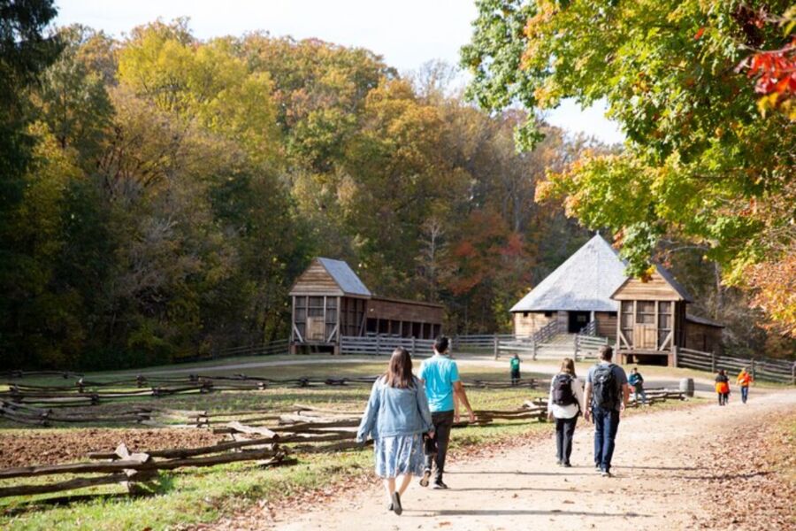 People walking along a dirt path in front of a rustic barn during a Mount Vernon day trip with a river cruise.
