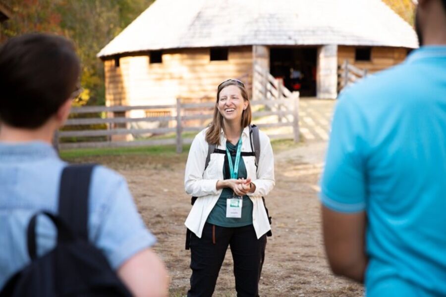 Woman engages with a group near a barn, part of a Mount Vernon day trip featuring a river cruise and guided tour.