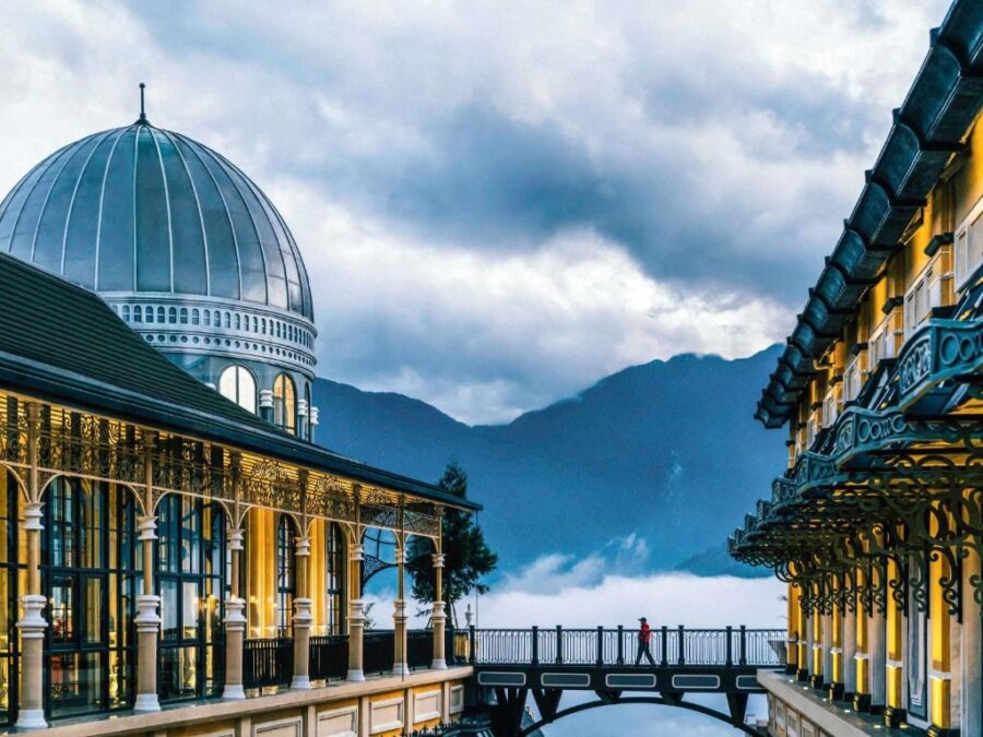 Luxury mountain hotel bridge with domed architecture, misty valley views, and dramatic cloudy sky.