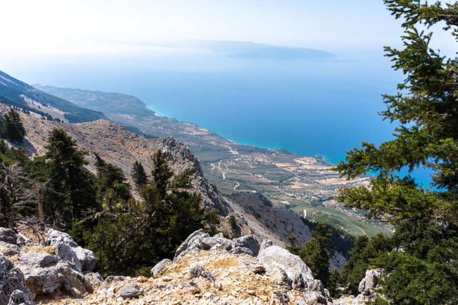 Mountainous landscape with rocky terrain, lush valleys, and turquoise sea under clear skies.