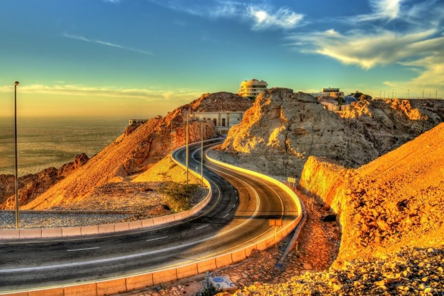 Mountain desert road at sunset winding through rocky hills near Al Ain viewpoint.